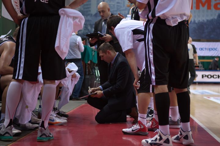 kneeling-basketball-coach-in-huddle-with-whiteboard Kneeling basketball coach diagraming play on whiteboard in huddle.